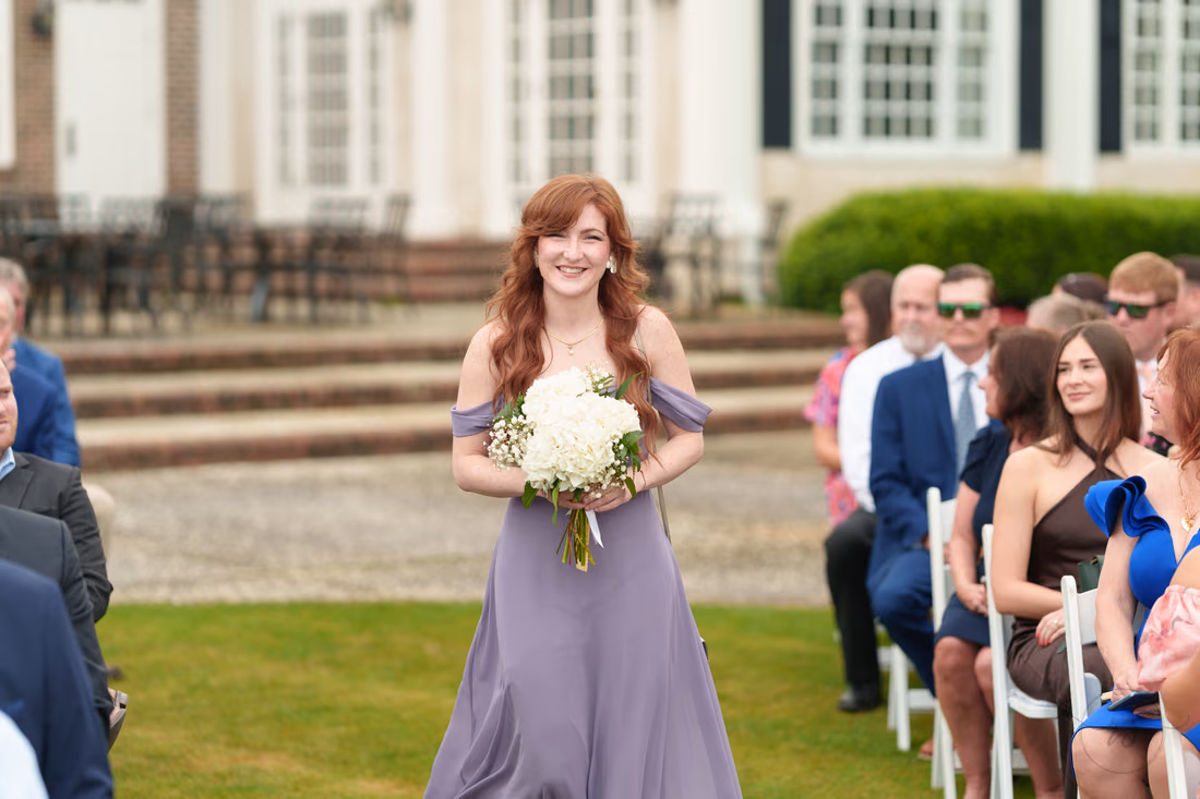 Bridesmaid in purple smiles as she walks down the aisle at Pawleys Plantation