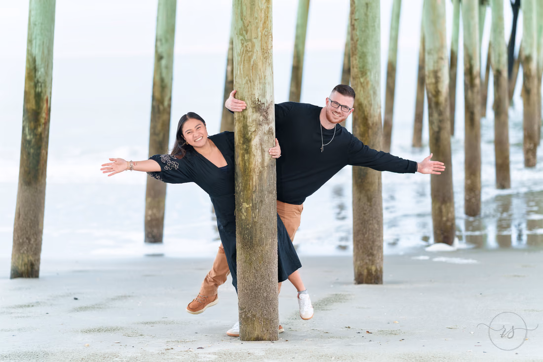 Couple playfully posing around a pier piling - Garden City Beach