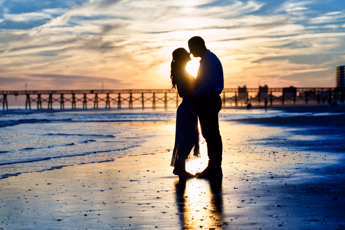 Couple silhouetted in a kiss at sunset by the pier - Cherry Grove Point