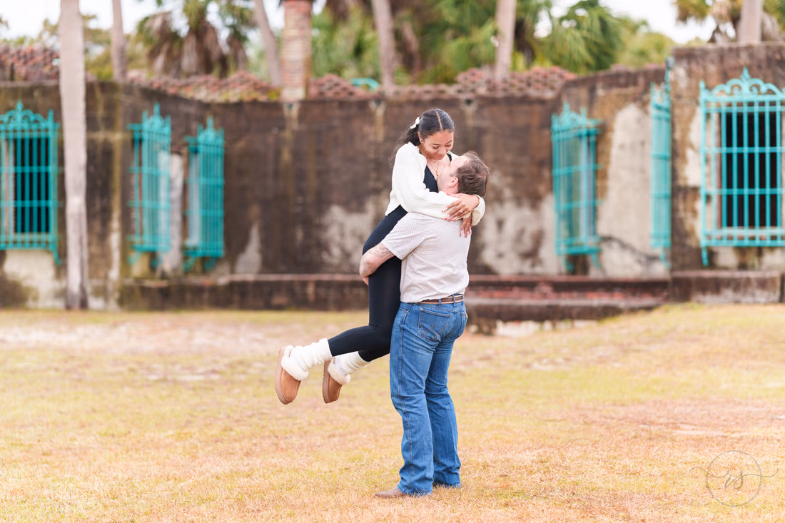 He lifts her for a kiss on the lawn in front of Atalaya Castle - Huntington Beach State Park