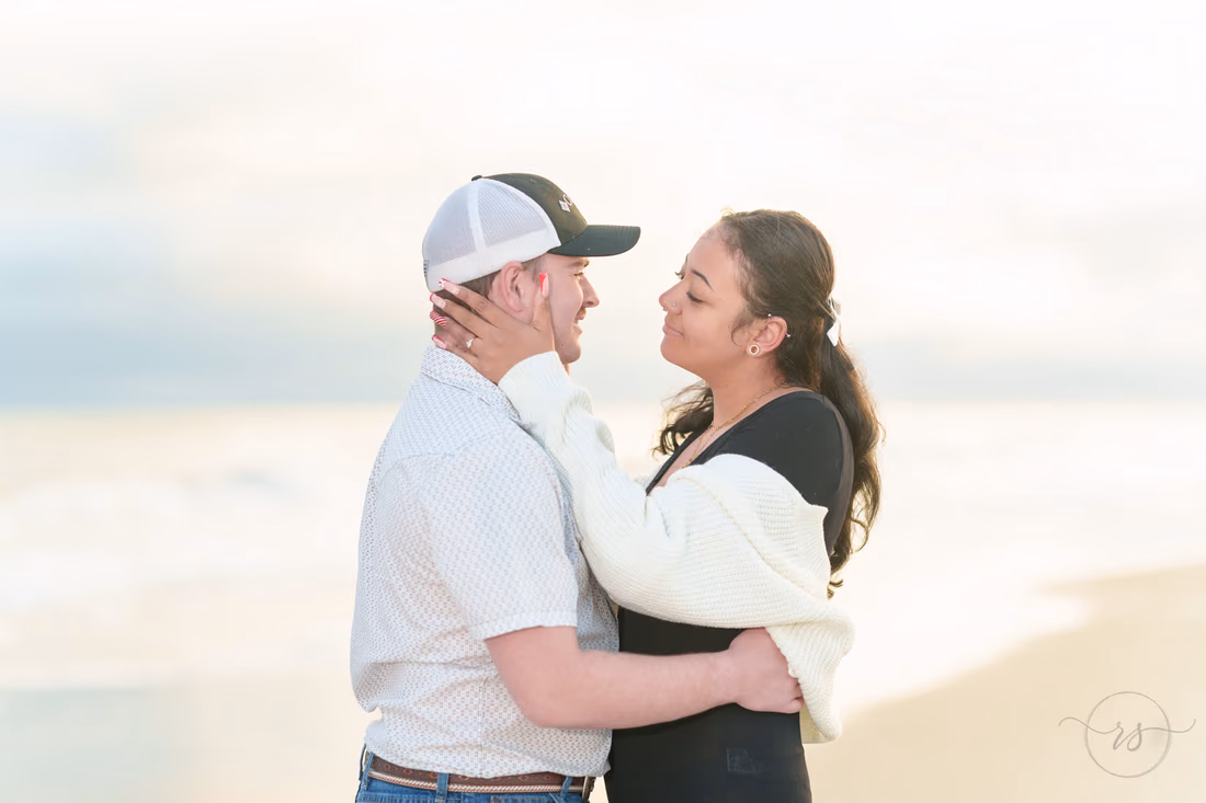 She holds his face as they hug on the beach - Huntington Beach State Park