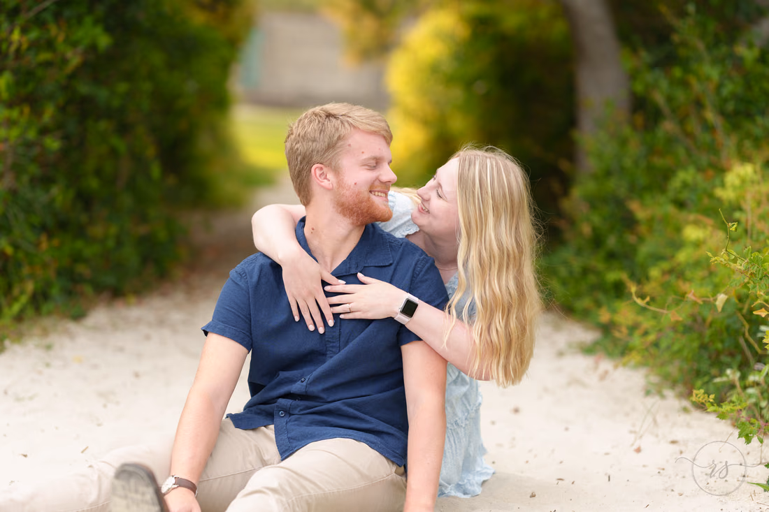 Couple sitting on the shaded sandy path, her arms around him - Huntington Beach State Park