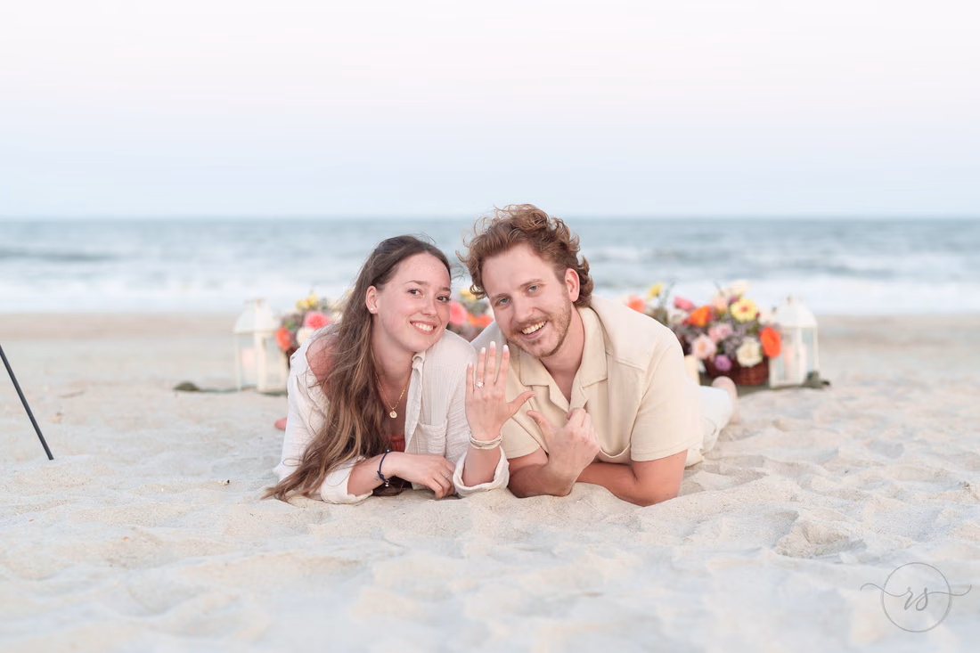 Couple lying in the sand showing off the ring in front of the proposal setup - Huntington Beach State Park