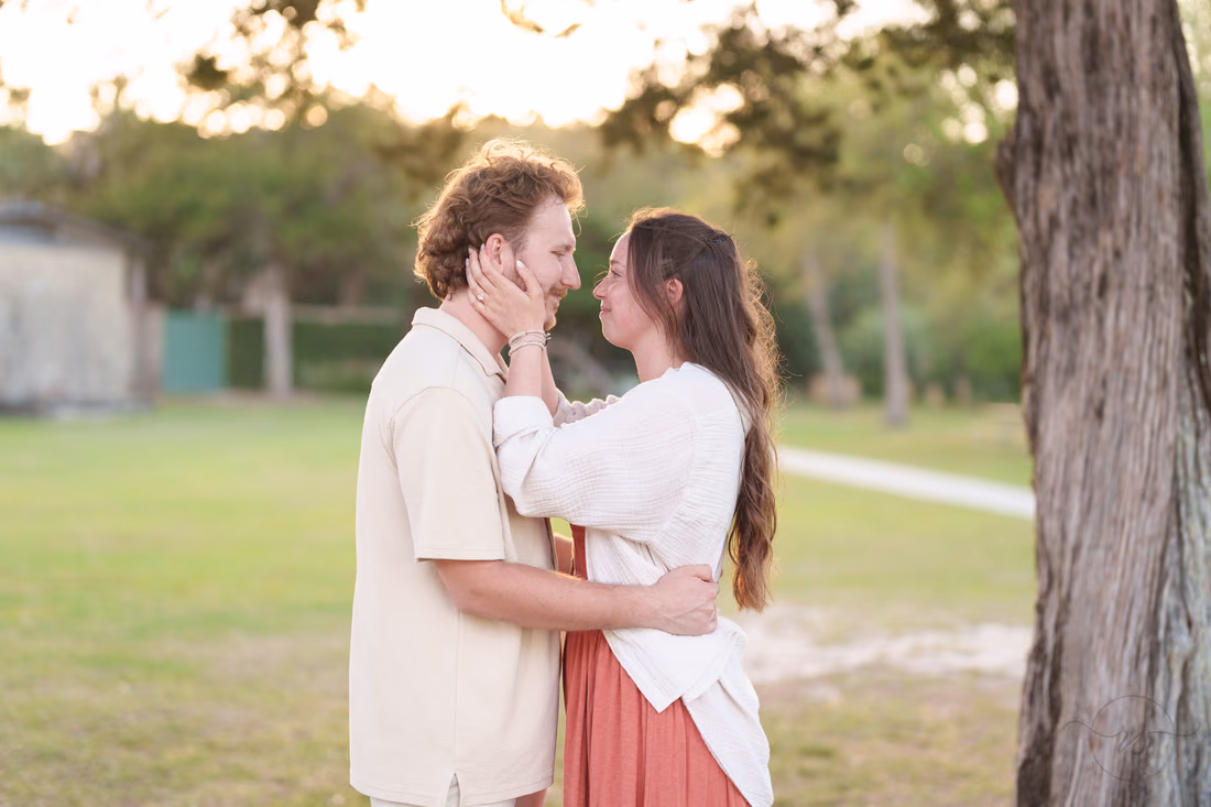 She holds his face on the lawn under the trees - Huntington Beach State Park