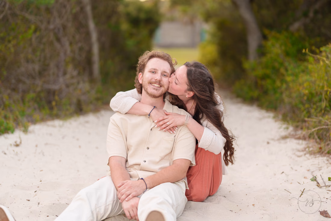 She kisses his cheek as they sit on the sandy path - Huntington Beach State Park