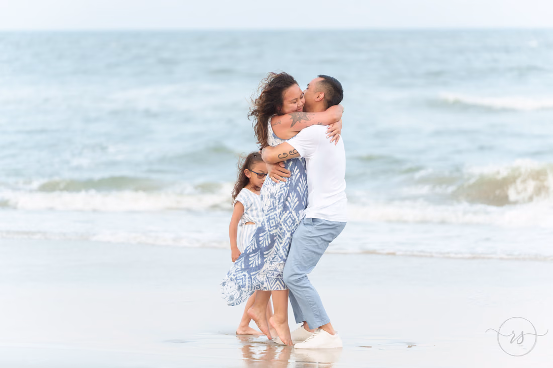 Couple hugging in the surf after the proposal as their daughter looks on - Huntington Beach State Park