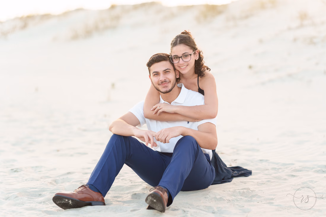 Couple sitting in the sand with her arms around him - Huntington Beach State Park