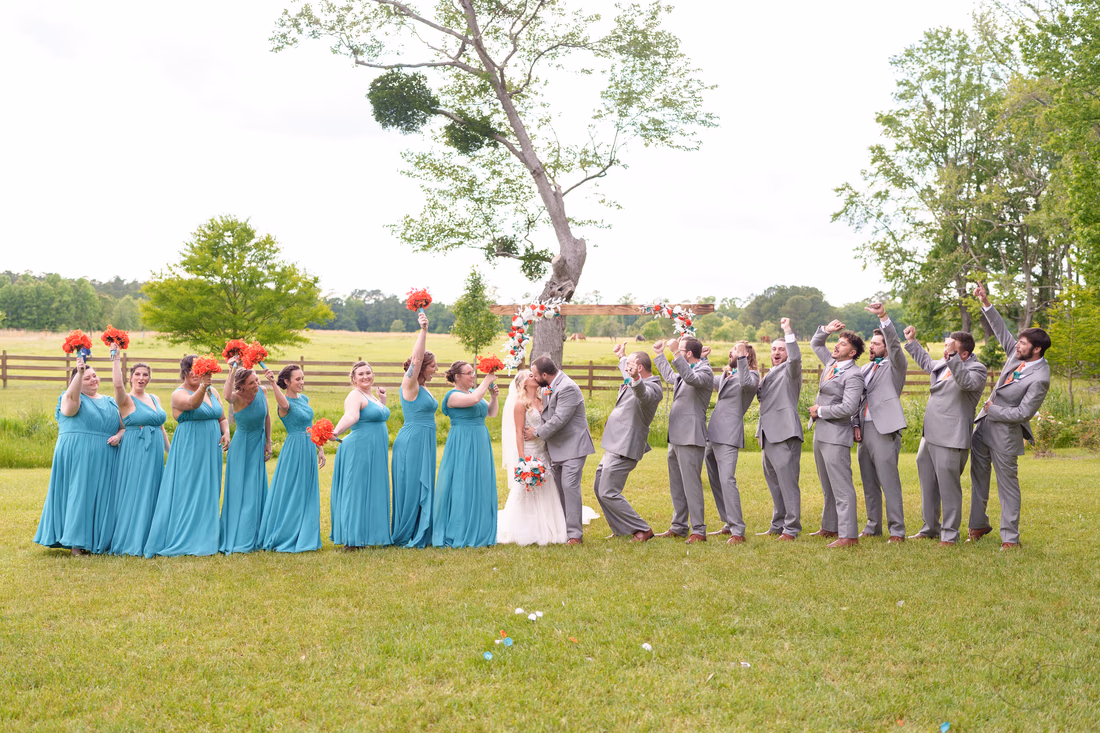 Wedding party cheering with bouquets raised in front of the pasture at Wildhorse at Parker Farms