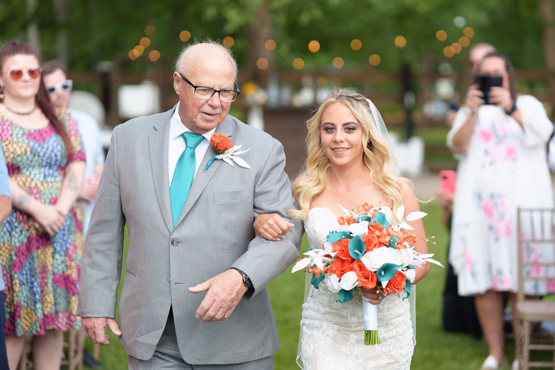 Bride and her father smiling as they walk arm in arm down the aisle at Wildhorse at Parker Farms