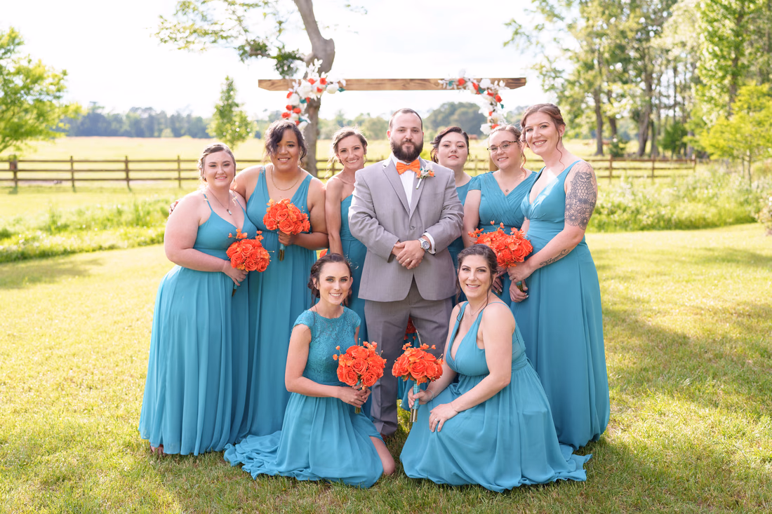 Groom posing with the bridesmaids in teal by the wooden arch at Wildhorse at Parker Farms