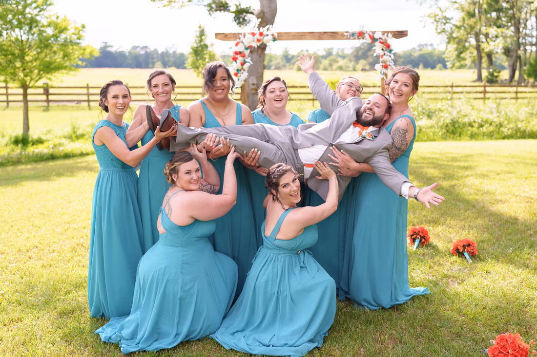 Bridesmaids holding the groom overhead and cheering by the ceremony arch at Wildhorse at Parker Farms