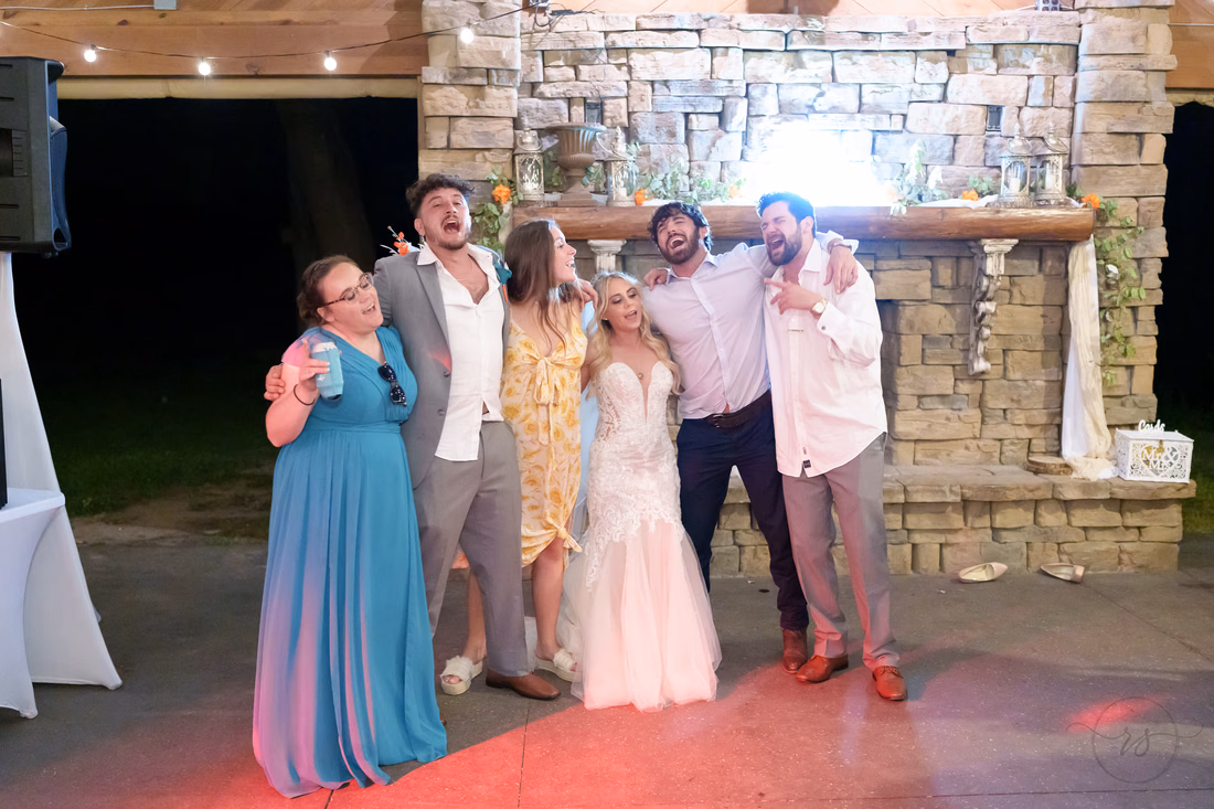 Bride and friends singing along arm in arm by the stone fireplace at Wildhorse at Parker Farms