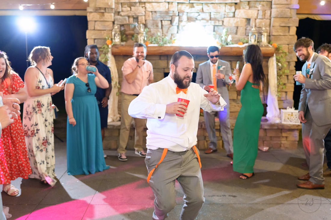 Groom dancing with a red cup in front of the stone fireplace at Wildhorse at Parker Farms