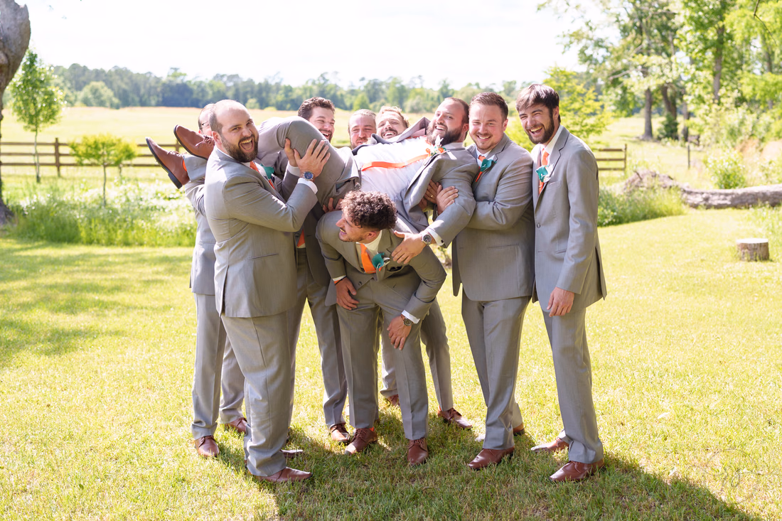 Groomsmen lifting the groom sideways over their heads by the pasture at Wildhorse at Parker Farms