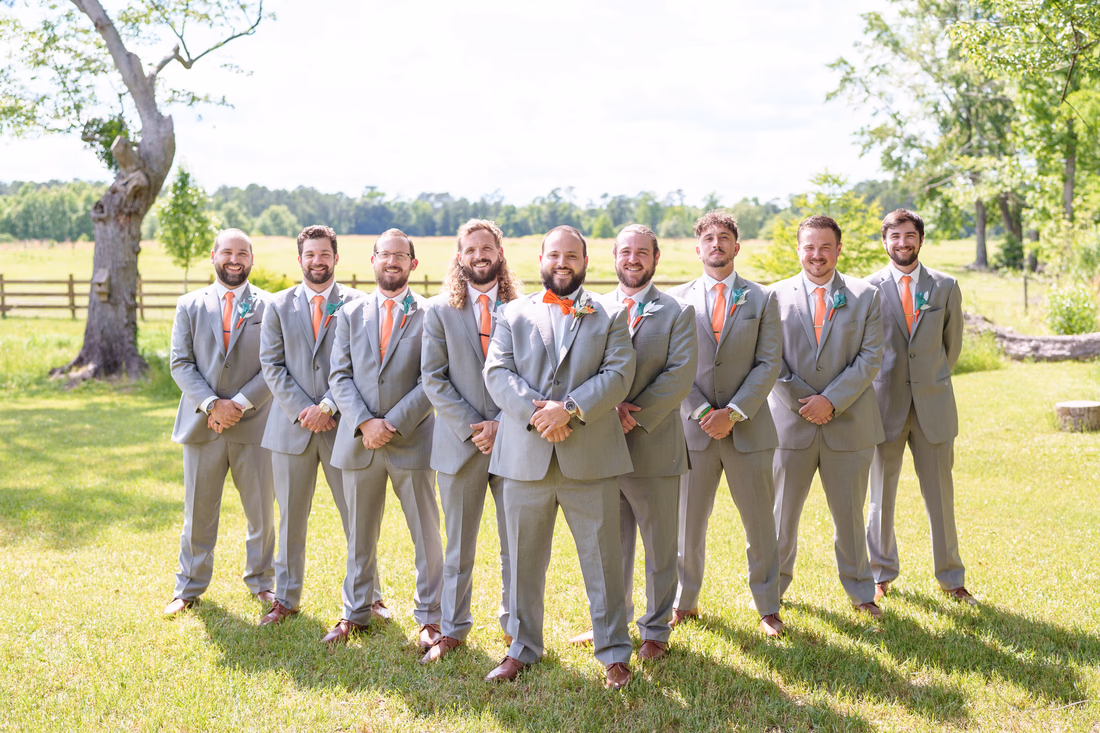 Groom and groomsmen in gray suits lined up in front of the pasture at Wildhorse at Parker Farms