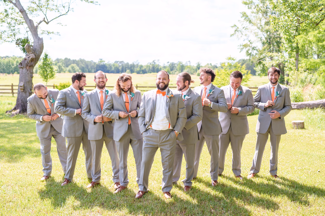 Groomsmen buttoning their jackets and glancing around in front of the pasture at Wildhorse at Parker Farms