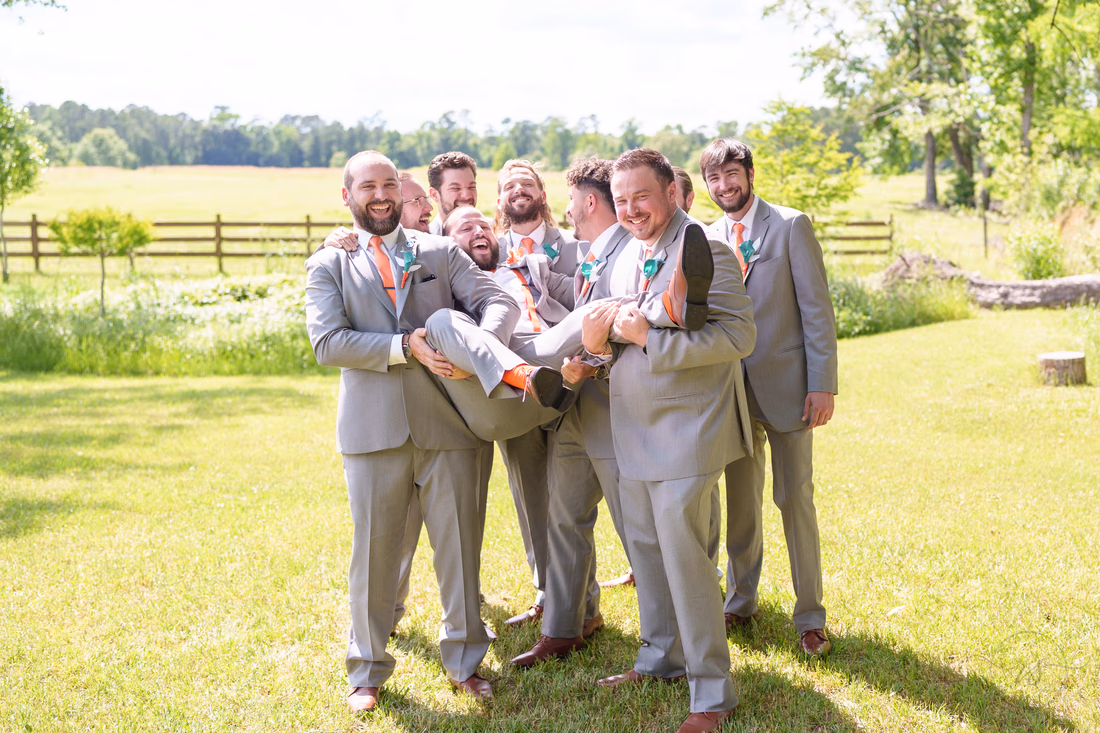 Groomsmen holding the groom up in their arms by the pasture at Wildhorse at Parker Farms