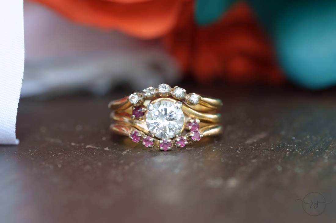 Close-up of the wedding band stack with pink stones on a wooden table at Wildhorse at Parker Farms