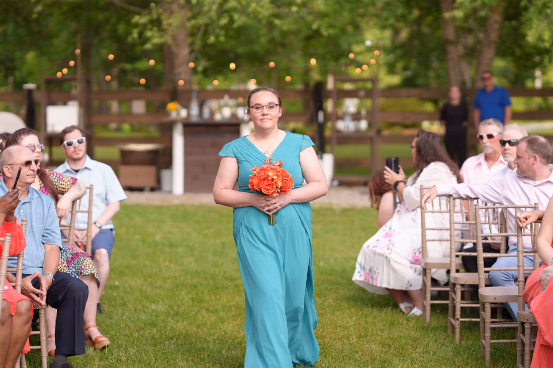 Bridesmaid in a teal dress walking to the ceremony between the guests at Wildhorse at Parker Farms
