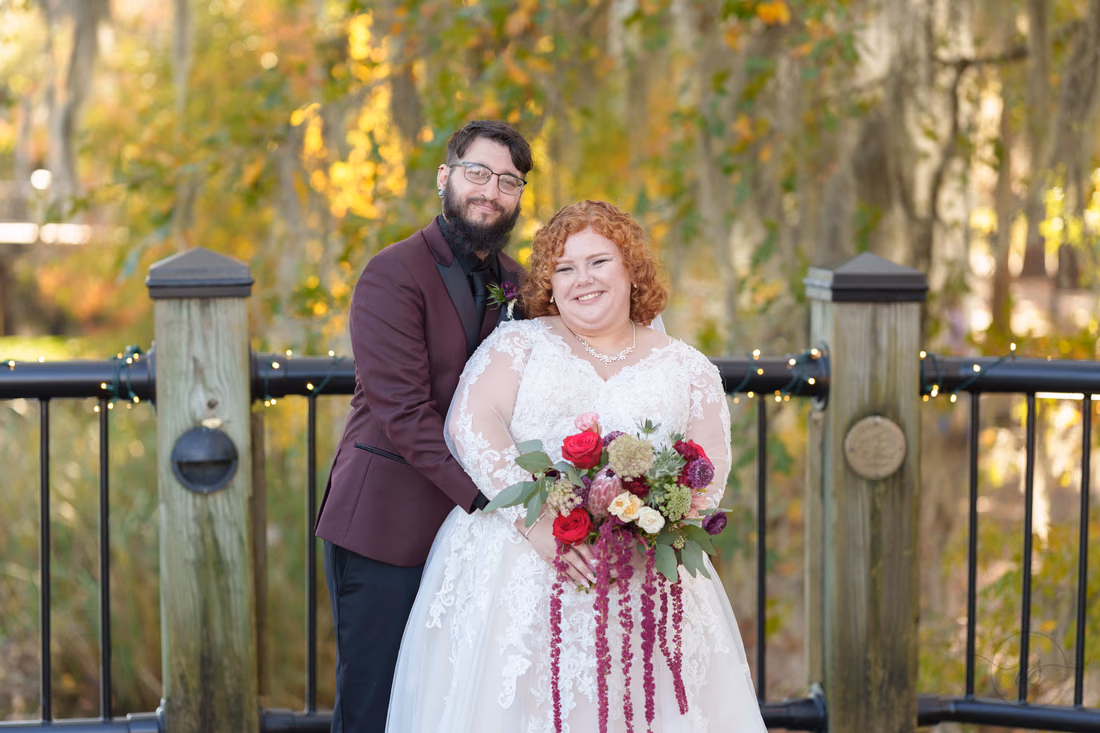 Couple smiling at the camera in front of golden fall trees on the Conway Riverwalk