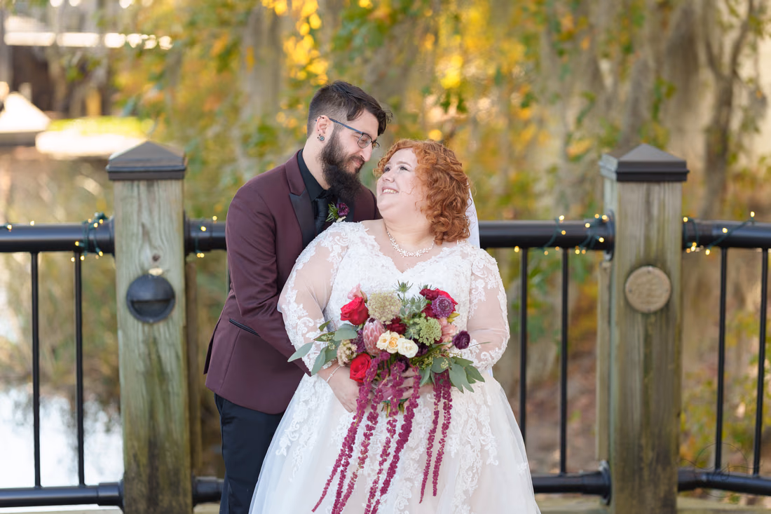 Groom leans in as the bride smiles up at him by the railing on the Conway Riverwalk