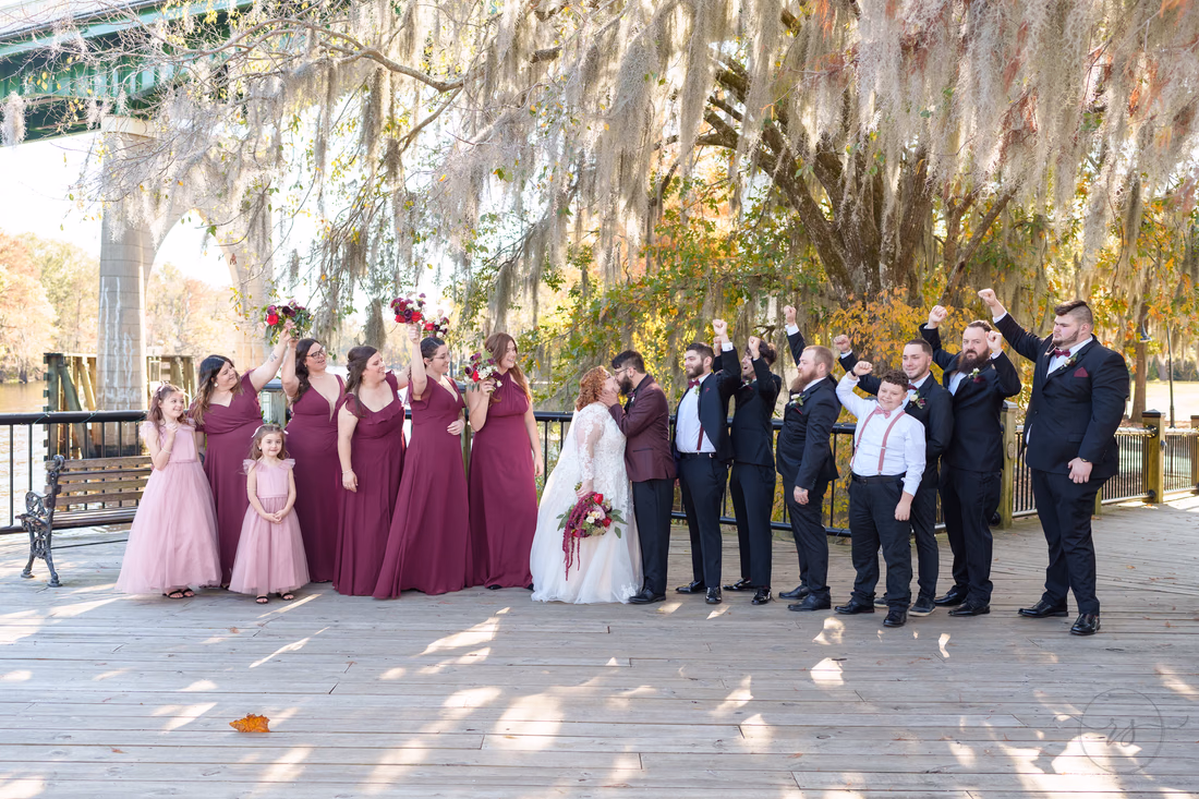 Wedding party cheering with bouquets raised under the mossy oaks on the Conway Riverwalk
