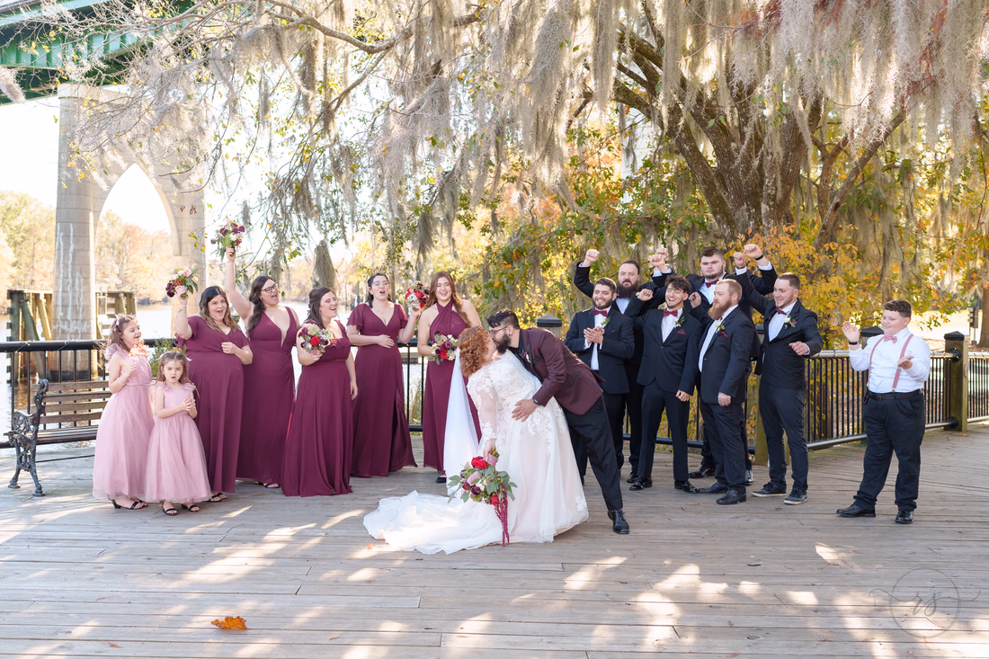 Groom dips the bride for a kiss as the wedding party cheers on the Conway Riverwalk
