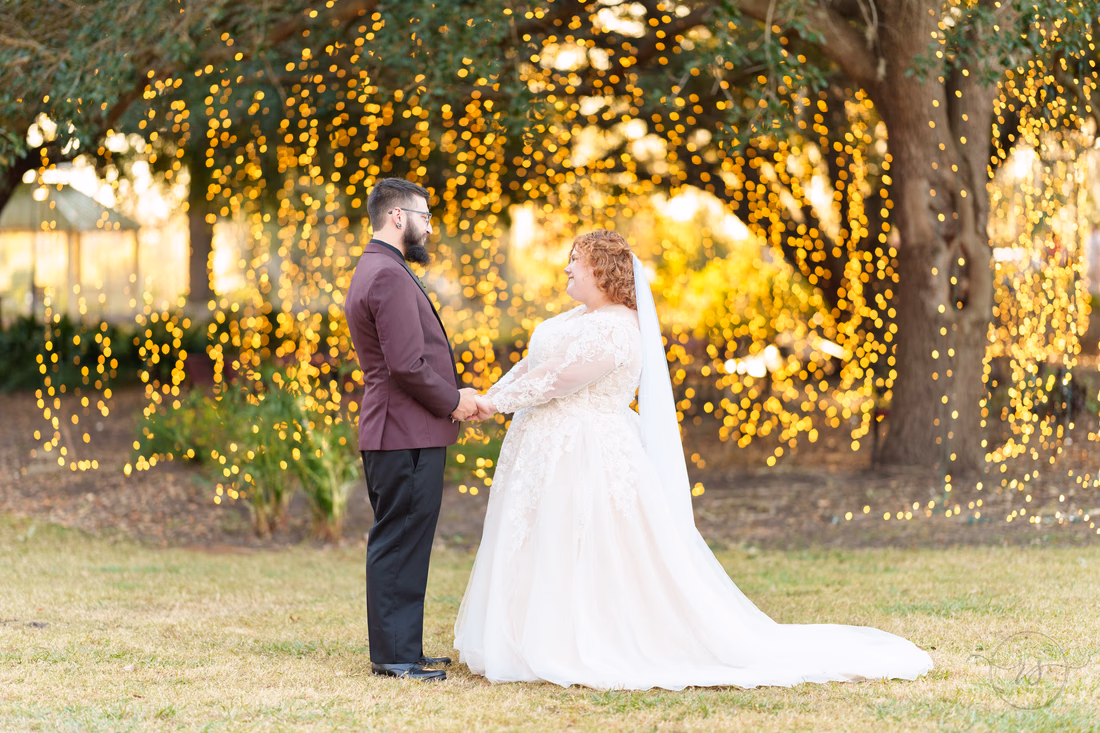 Bride and groom hold hands in front of glowing hanging lights on the Conway Riverwalk
