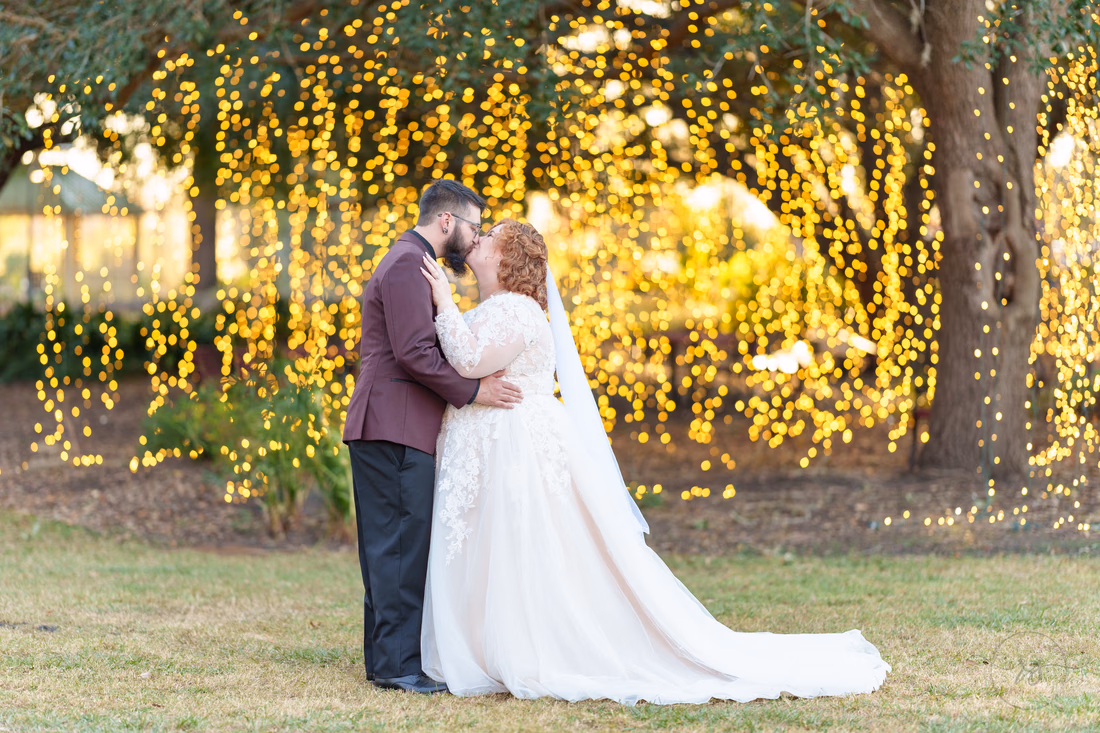 Couple kissing in front of a curtain of hanging lights in the trees on the Conway Riverwalk