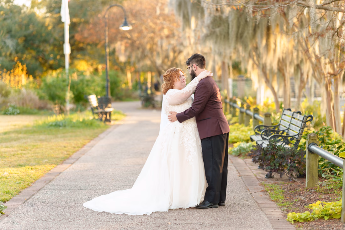 Bride and groom embrace on the moss-covered path lined with benches on the Conway Riverwalk