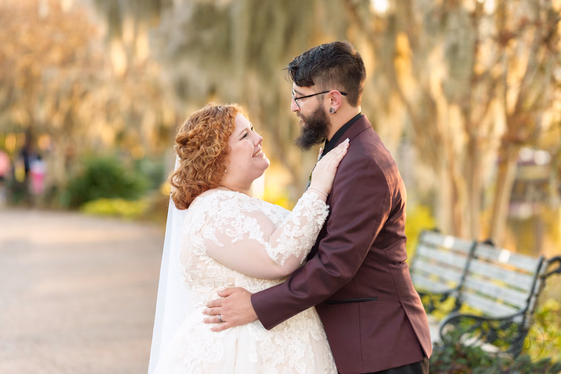 Bride gazes up at the groom by a park bench under hanging moss on the Conway Riverwalk