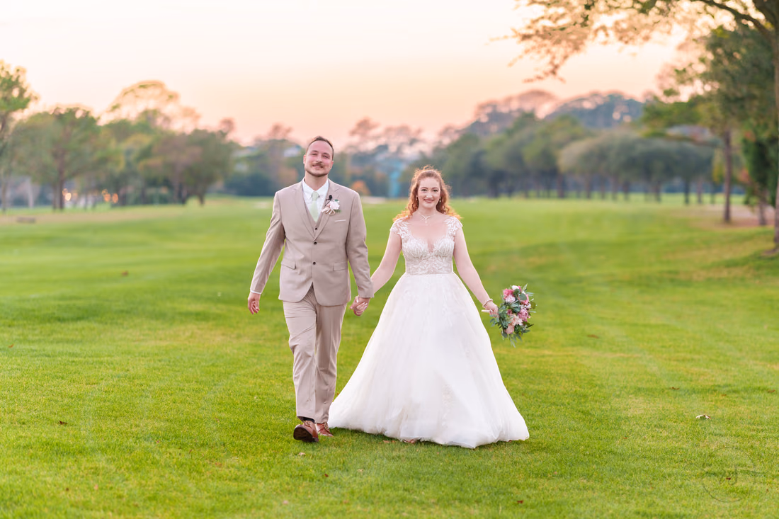 The bride and groom walk hand in hand across the golf course at Pine Lakes Country Club