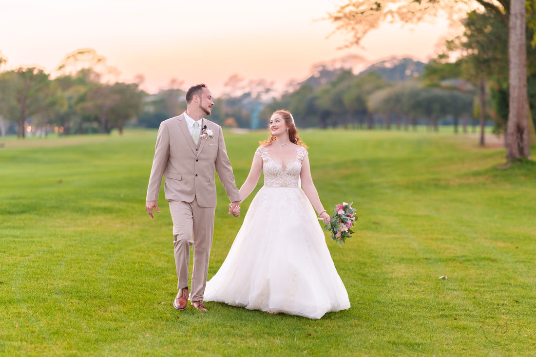 The bride smiles at the groom as they walk across the fairway at Pine Lakes Country Club