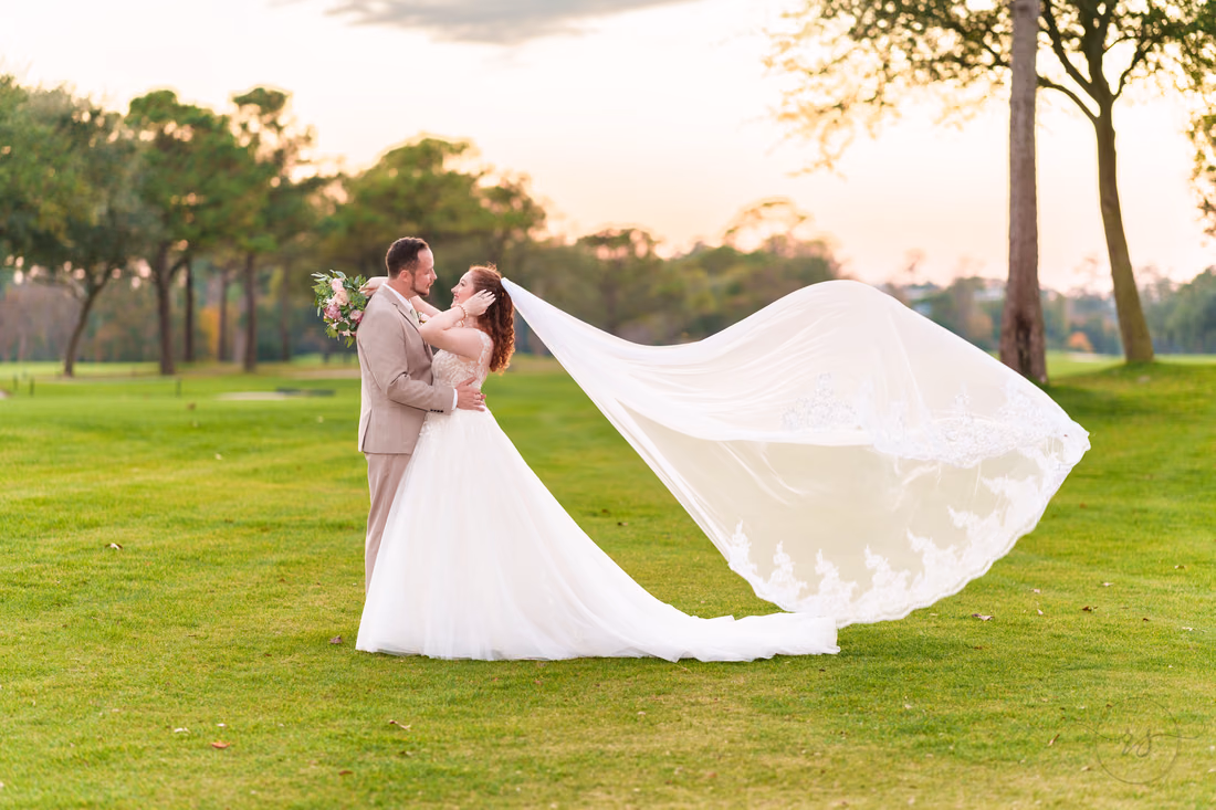 The bride's veil flies in the wind as the couple kisses on the golf course at Pine Lakes Country Club