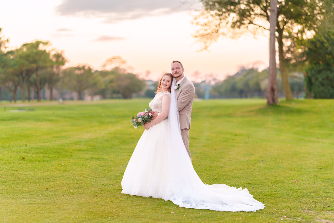 The bride and groom pose on the fairway under a pink sky at Pine Lakes Country Club
