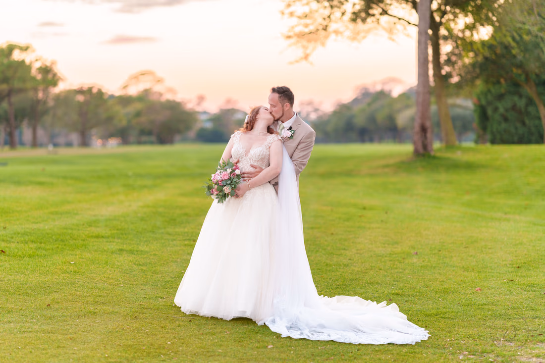The groom kisses the bride's head on the golf course at dusk at Pine Lakes Country Club