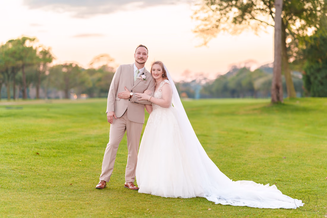 The bride hugs the groom's arm on the golf course at dusk at Pine Lakes Country Club