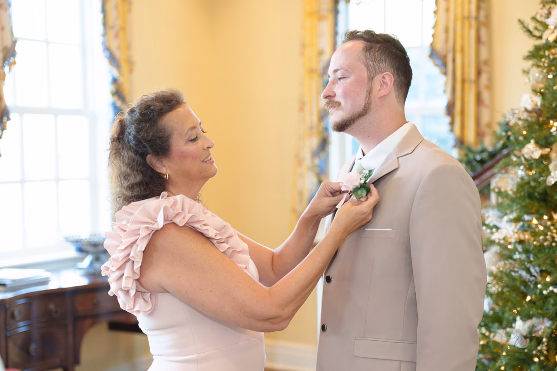 A woman pins a boutonniere on the groom at Pine Lakes Country Club
