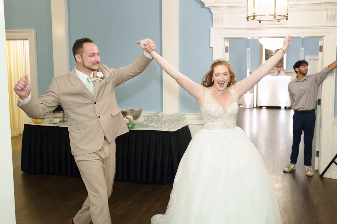 The bride and groom raise their arms as they enter the reception at Pine Lakes Country Club