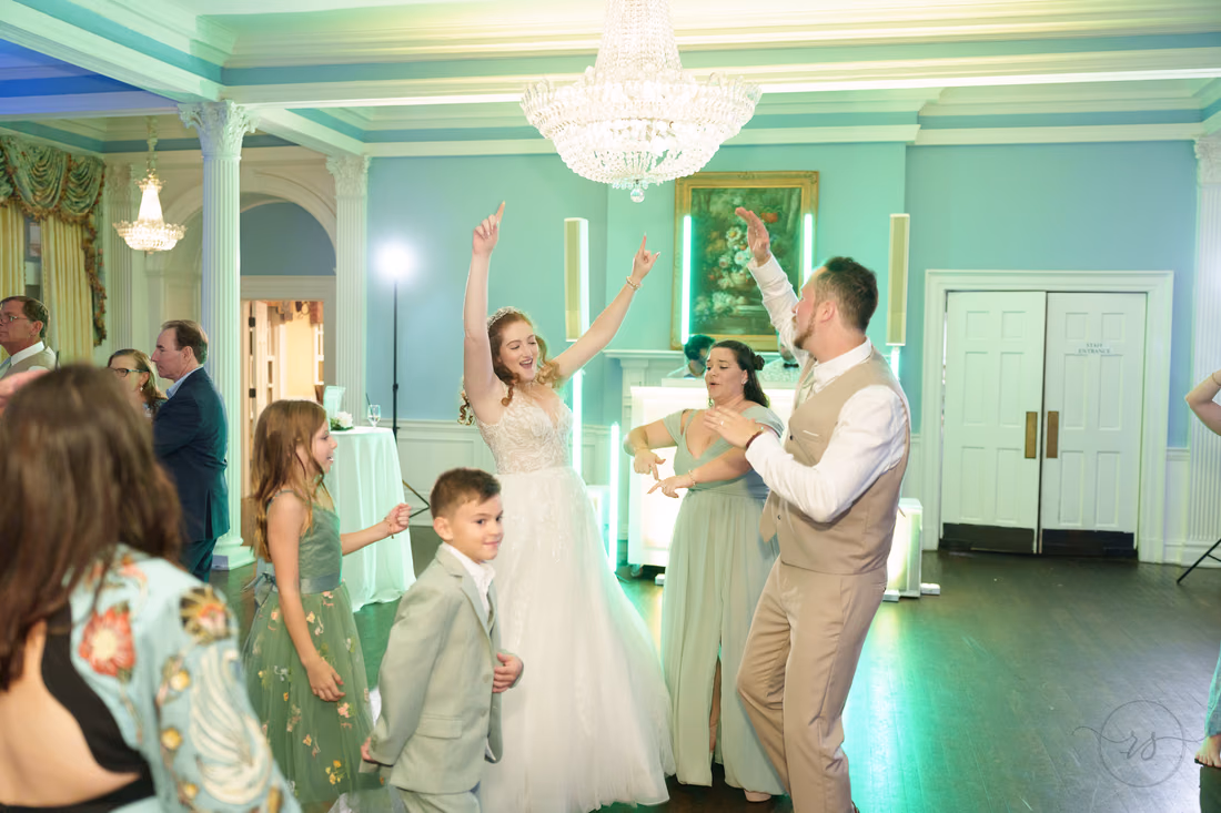 The bride and groom throw their hands up with guests under green lights at Pine Lakes Country Club