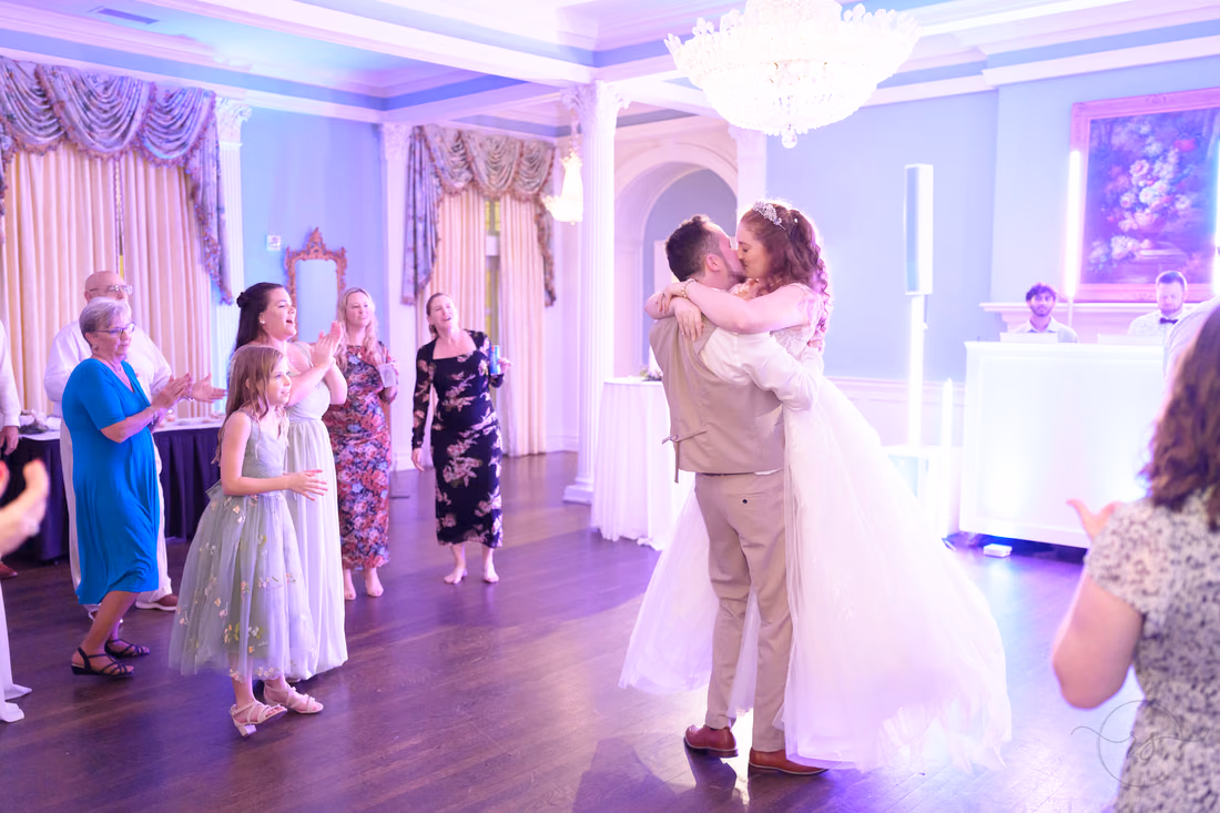 The bride and groom hug as guests dance around them at Pine Lakes Country Club