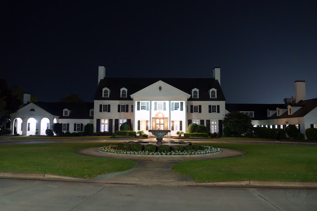 The clubhouse lit up at night with the fountain in front at Pine Lakes Country Club