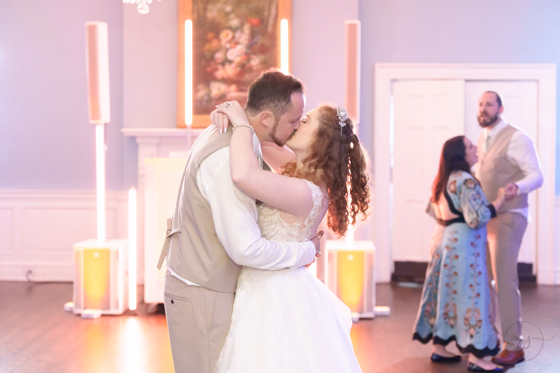 The bride and groom kiss on the dance floor as another couple dances behind them at Pine Lakes Country Club