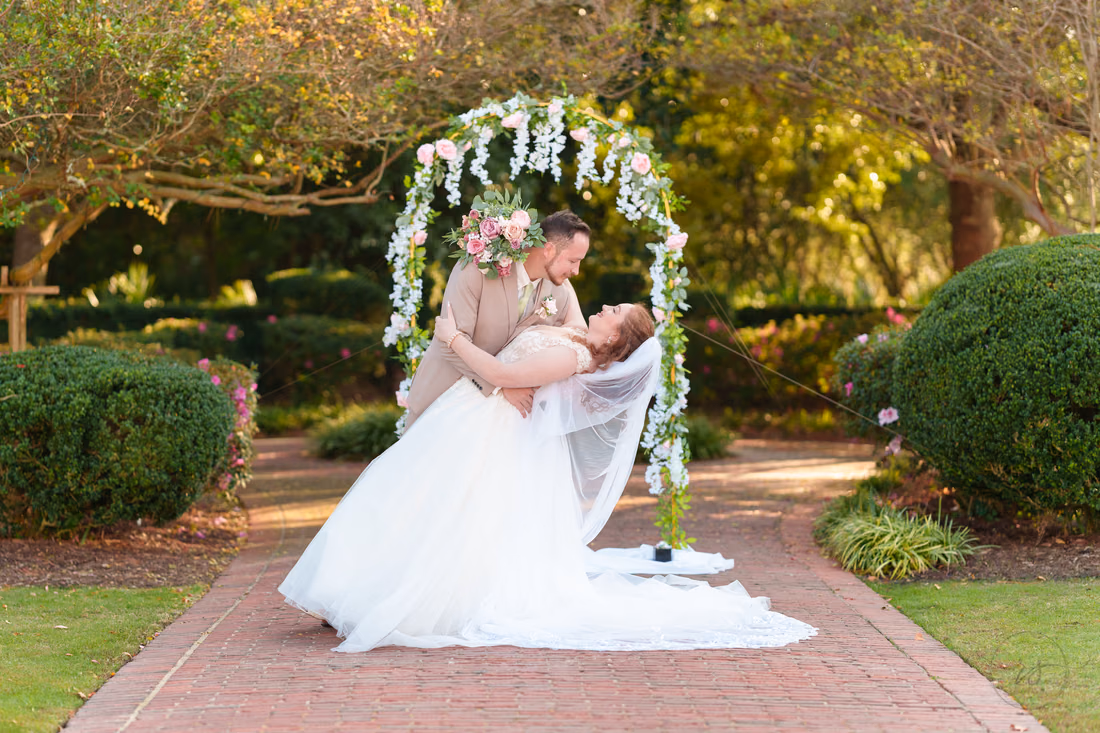 The groom dips the bride under the flower arch at Pine Lakes Country Club