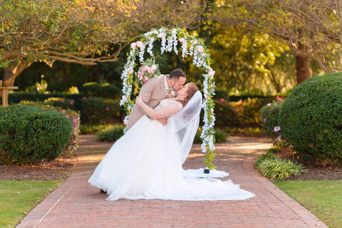 The groom dips the bride for a kiss under the flower arch at Pine Lakes Country Club
