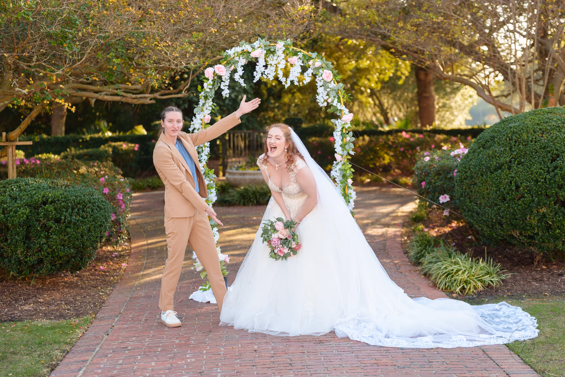 A groomsman points at the bride as she laughs under the flower arch at Pine Lakes Country Club
