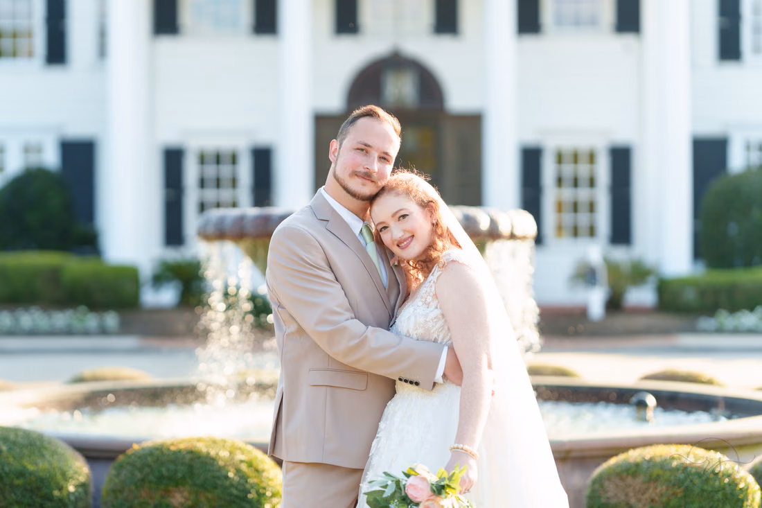 The bride leans on the groom's chest by the fountain at Pine Lakes Country Club