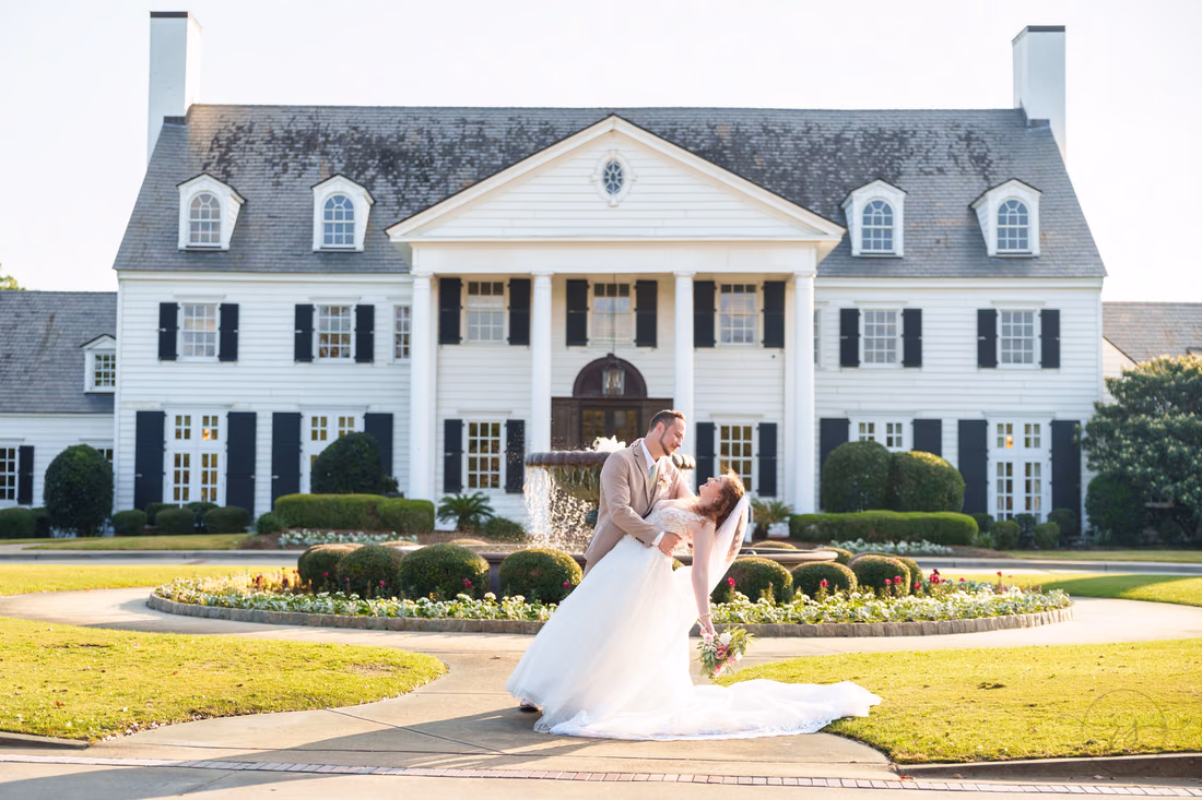 The groom dips the bride in front of the white columned clubhouse at Pine Lakes Country Club