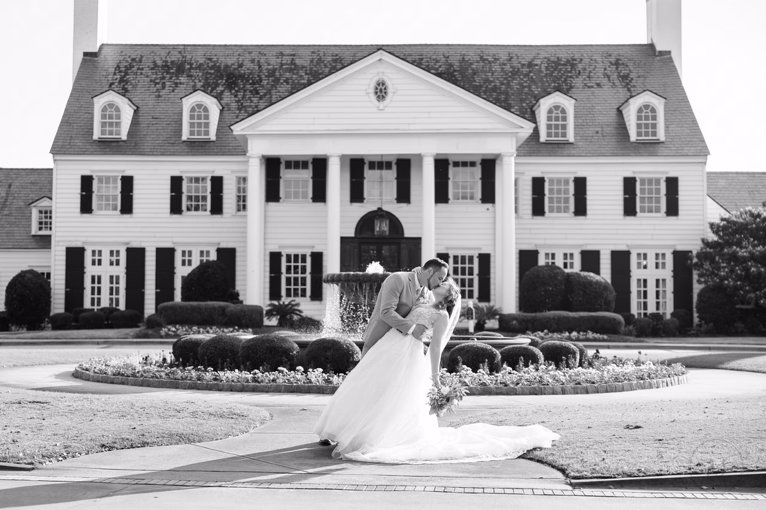 Black and white photo of the groom dipping the bride in front of the clubhouse at Pine Lakes Country Club