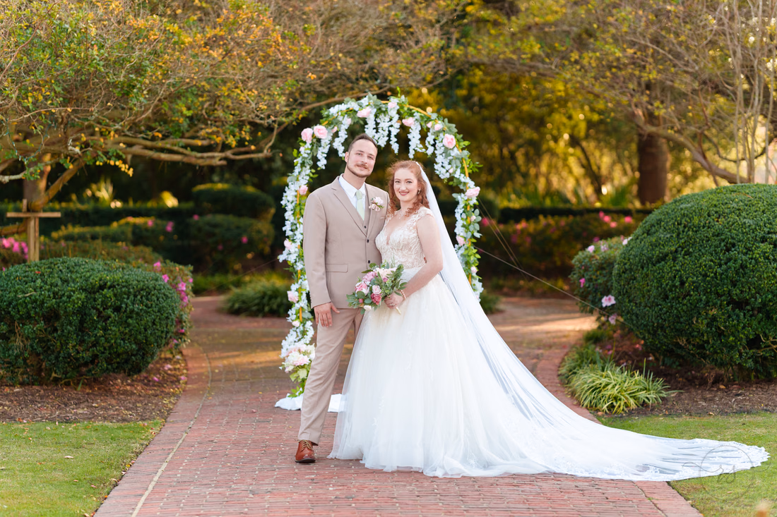 The bride and groom pose together under the flower arch at Pine Lakes Country Club